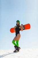 jovem mulher bonita posando com uma prancha de snowboard em uma pista de esqui foto