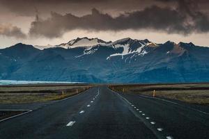 estrada de asfalto reta com tempestade sobre montanha em dia sombrio na islândia foto