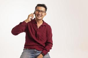 homem asiático inteligente usando smartphone no fundo do estúdio, bonito jovem asiático sorrindo alegremente na camisa formal. usando um smartphone para trocar ou conversar foto