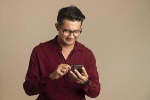 homem asiático inteligente usando smartphone no fundo do estúdio, bonito jovem asiático sorrindo alegremente na camisa formal. usando um smartphone para trocar ou conversar foto