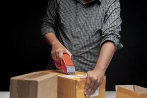 um homem está empacotando uma pequena caixa de seu negócio online em seu quarto em casa. foto