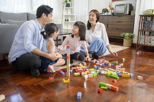 família asiática com crianças brincando e construindo torre de blocos de brinquedo de madeira coloridos na sala de estar em casa, jogo educacional. foto