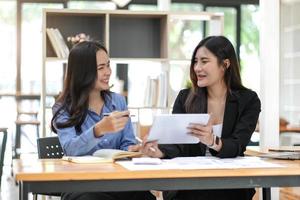 duas muito jovem empresária asiática sentada na mesa com o laptop fazendo papelada juntos discutindo o relatório financeiro do projeto. conceito de colaboração de negócios corporativos. foto