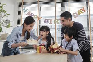 feliz família tailandesa asiática, jovem linda garota surpresa com bolo de aniversário, presente, soprar vela e comemorar festa com pais e irmãos juntos na mesa de jantar, evento especial doméstico doméstico de bem-estar. foto