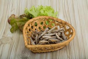 seca a anchova em uma cesta no fundo de madeira foto