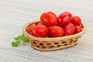 tomate cereja em uma cesta em fundo de madeira foto