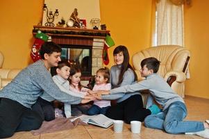 feliz jovem grande família em casa por uma lareira na sala de estar quente em dia de inverno. mão nas mãos. foto