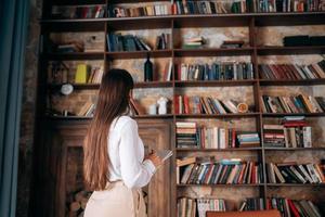 jovem mulher bonita com óculos segurando um notebook e olhando para a estante foto