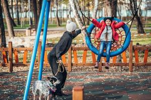 mãe balança a filha em um balanço no parque outono foto