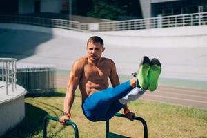 homem forte fazendo exercícios em barras irregulares no ginásio de rua ao ar livre. foto