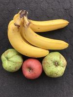 um cacho de bananas, duas goiabas e 1 maçã em um fundo escuro foto