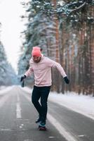 skatista em pé na estrada no meio da floresta, cercado por neve foto