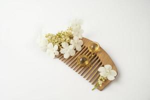 cápsulas douradas de vitaminas de óleo natural para cabelo deitado em um pente de madeira foto