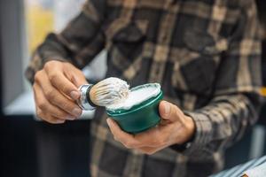 o mestre tem um pincel e espuma de barbear na mão foto