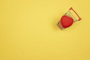 um coração vermelho encontra-se em um carrinho de compras em um fundo amarelo. conceito de dia dos namorados foto