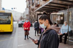 jovem mulher usando máscara cirúrgica ao ar livre no ponto de ônibus na rua foto