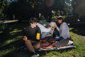 companhia de belos jovens e cachorro almoçando ao ar livre. foto