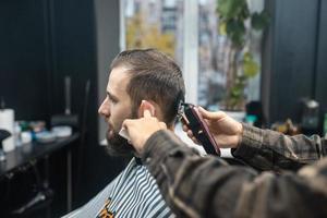 mestre em barbearia faz corte de cabelo masculino com máquina de cortar cabelo foto