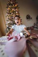 menina dando um presente no fundo de uma árvore de natal foto