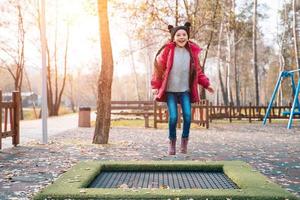 menina da escola feliz pulando em um pequeno trampolim no parque foto