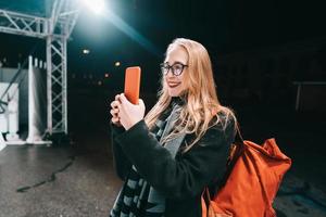 mulher loira com smartphone à noite na rua. foto