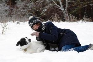 retrato de mulher jovem e bonita com seu cachorro preto e branco em um fundo de floresta de inverno nevado. foto