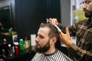 alegre jovem barbudo cortando o cabelo pelo cabeleireiro na barbearia foto