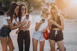 quatro mulheres atraentes estão de pé no estacionamento com smartphones foto