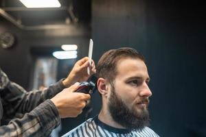 mestre em barbearia faz corte de cabelo masculino com máquina de cortar cabelo foto