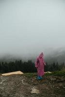 garota alpinista atraente em uma capa de chuva rosa fica em uma montanha foto