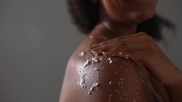 mulher afro-americana esfrega esfoliação na pele do ombro no banheiro foto