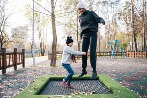 mãe e filha pulando juntos no trampolim no parque outono foto