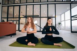 duas jovens meditando em pose de lótus com as mãos em namastê. foto