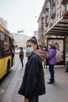 jovem mulher usando máscara cirúrgica ao ar livre no ponto de ônibus na rua foto