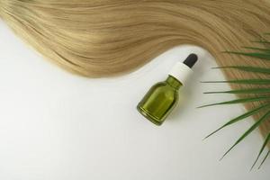 um óleo natural ou soro para cuidados com os cabelos e uma camada de cabelo loiro deitado sobre um fundo branco foto