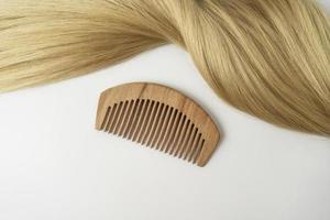 um fio de cabelo loiro com um pente de madeira deitado sobre um fundo branco foto