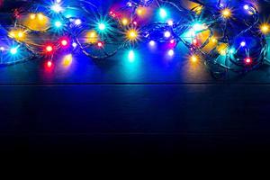 fundo de luzes de natal com espaço de texto livre. brilhantes luzes de natal coloridas em fundo de madeira. ano Novo. luzes multicoloridas para decorar o evento. foto