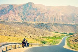 ciclista masculino caucasiano empurra sua bicicleta de turismo pesada para cima em calor extremo ao ar livre nas montanhas. conceito de estilo de vida de aventura de ciclismo. ciclo difícil subida e determinação foto