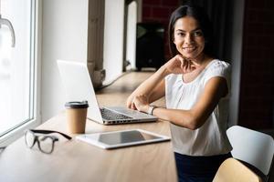 procurando por nova solução. empresária bonita jovem pensativa em copos trabalhando no laptop enquanto está sentado no seu local de trabalho