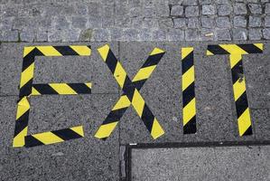 a palavra saída escrita com fita de barreira amarela e preta em uma calçada. foto