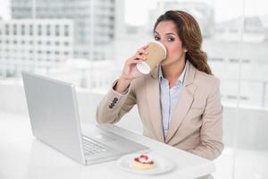 empresária tomando café na mesa na frente do laptop