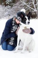 retrato de mulher jovem e bonita com seu cachorro preto e branco em um fundo de floresta de coníferas de inverno. foto