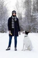 retrato de uma bela jovem sorridente com seu cachorro preto e branco em um fundo de floresta de inverno. foto