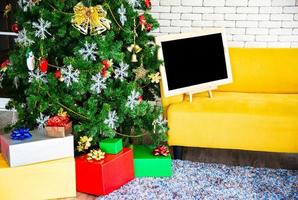 conceito de férias de natal e ano novo. decoração de árvores de natal com fitas de placa preta bolas flocos de neve e enfeites e caixas de presente sobre parede de tijolo branco prepare-se para festa noturna foto