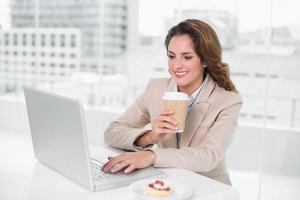 empresária tomando café na mesa dela usando laptop foto