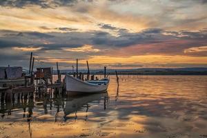 incrível pôr do sol colorido em um lago com um barco em um cais de madeira. visão horizontal foto