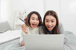 duas mulheres felizes fazendo compras online com cartão de crédito e laptop em casa foto