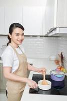 jovem mulher cozinhando em sua cozinha em pé perto do fogão. estilo de vida saudável. foto