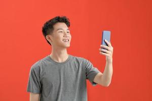 um homem asiático com jaqueta marrom fazendo uma selfie sobre fundo vermelho isolado foto