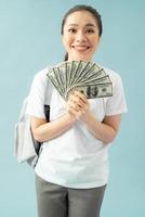 aluna feliz isolada em fundo azul, mantenha fã de dinheiro em notas de dólar fazendo gesto de vencedor foto